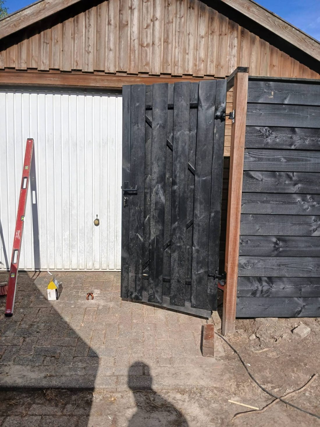 Zwarte houten poort opgehangen naast de schutting
